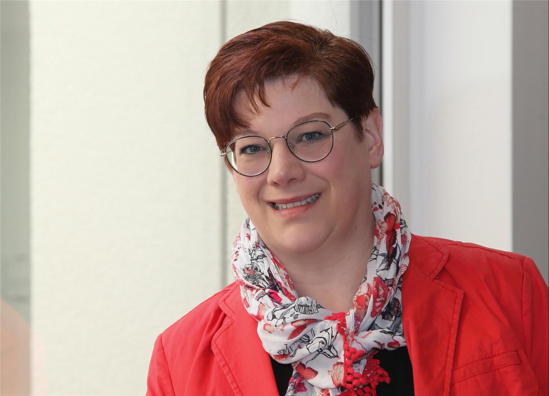 Frau mit Brille und kurzen dunklem Haar, rotes Oberteil, lächelt in die Kamera