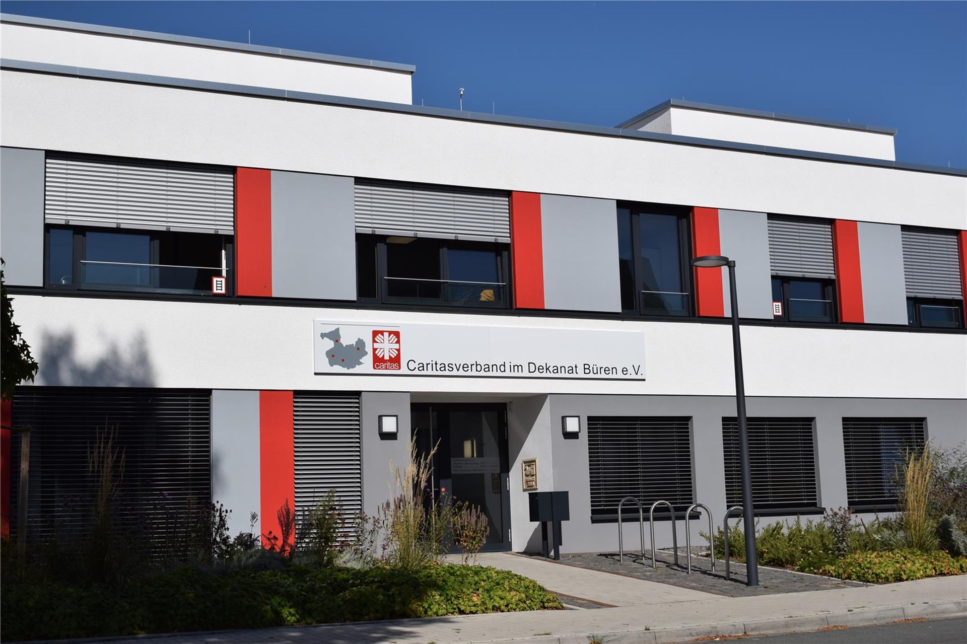 moderner Flachbau mit grau-weißer Aussenfassade und roten Akzenten, Haupteingang aus Glas darüber die Aufschrift Caritasverband im Dekanat Büren e. V.