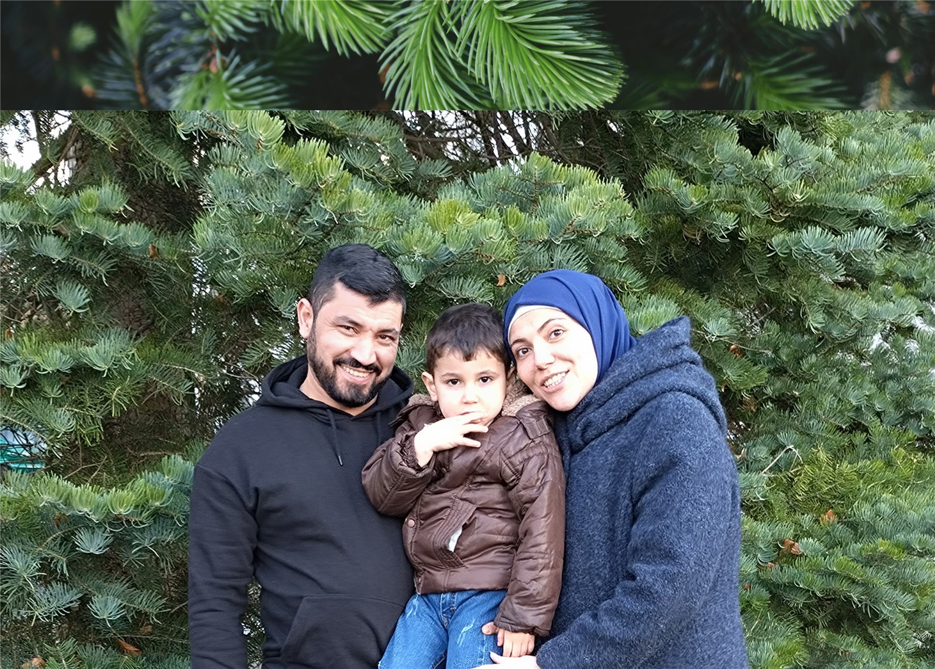 Vater, Mutter, Kind: eine junge Familie aus Beirut stehen vor einer Tannen-Hecke in einem Garten. Die beiden Elternteile tragen den Sohn in ihrer Mitte