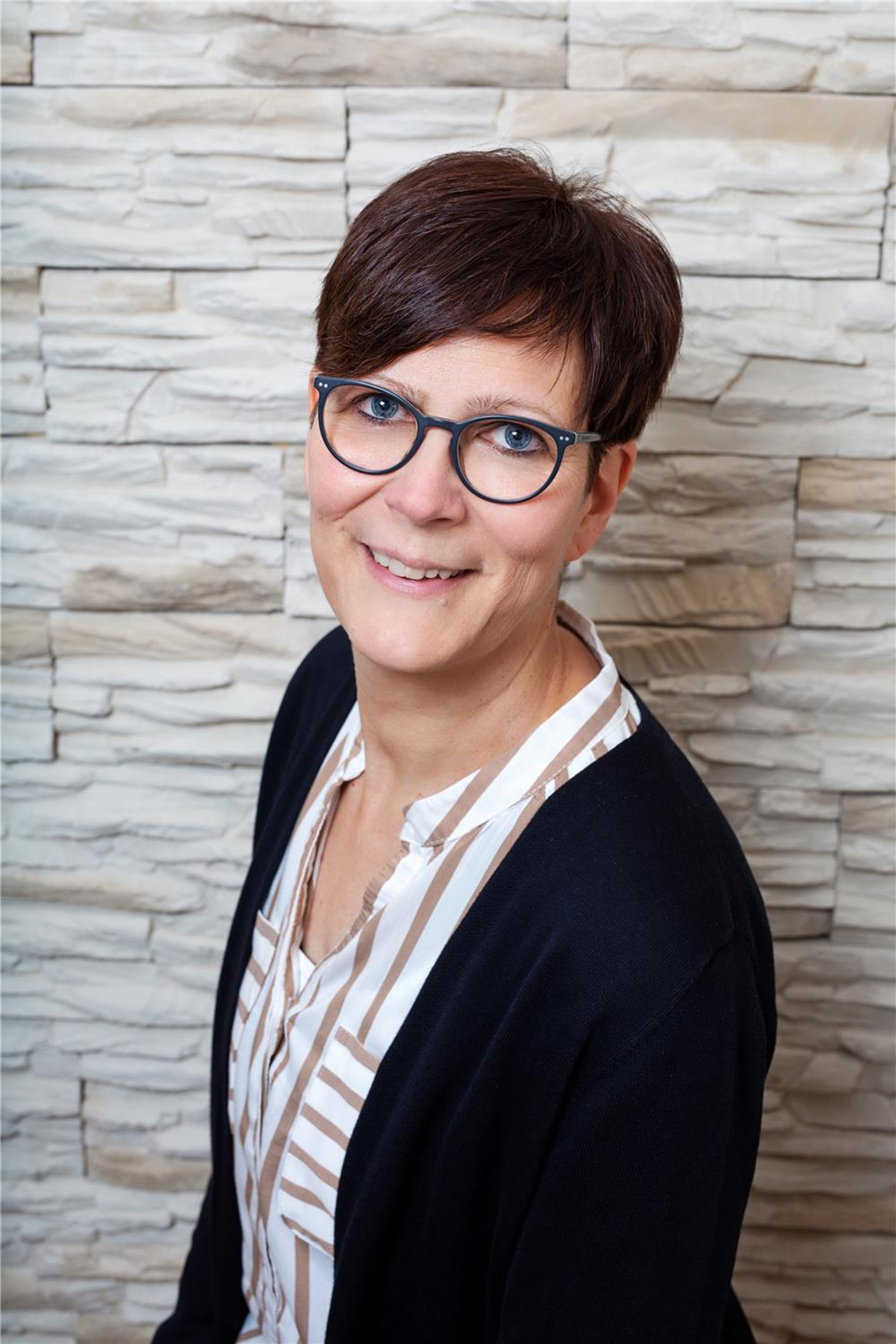junge Frau mit dunklem kurzen Haar, dunkler Jacke, heller Bluse und Brille