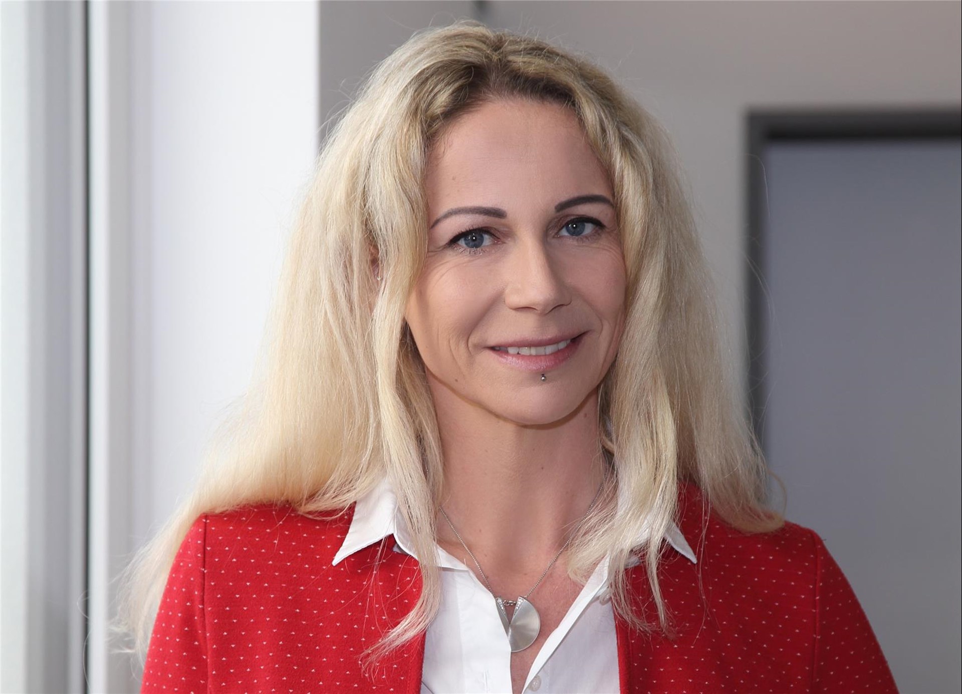 Frau mit langem blonden Haar und rotem Oberteil lächelt in die Kamera