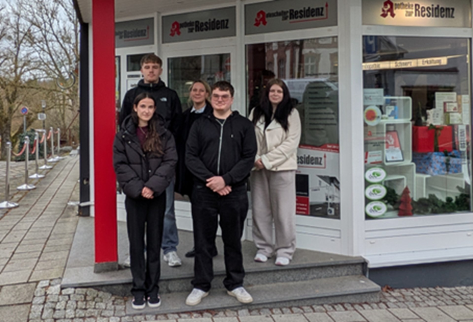 drei weibliche Jugendliche und ein junger Mann stehen vor der Residenz Apotheke. Die Lehrerin steht hinter der Gruppe. 