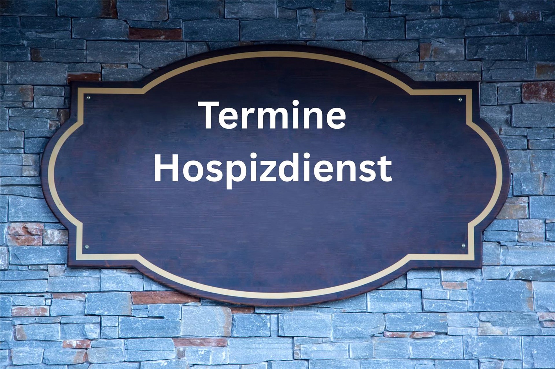 blau-grau geschieferte Wand, darauf ein Türschild mit einer weißen Aufschrift Termine Hospizdienst